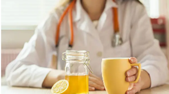 Médica com uma xícara e do lado um pote com mel e limão